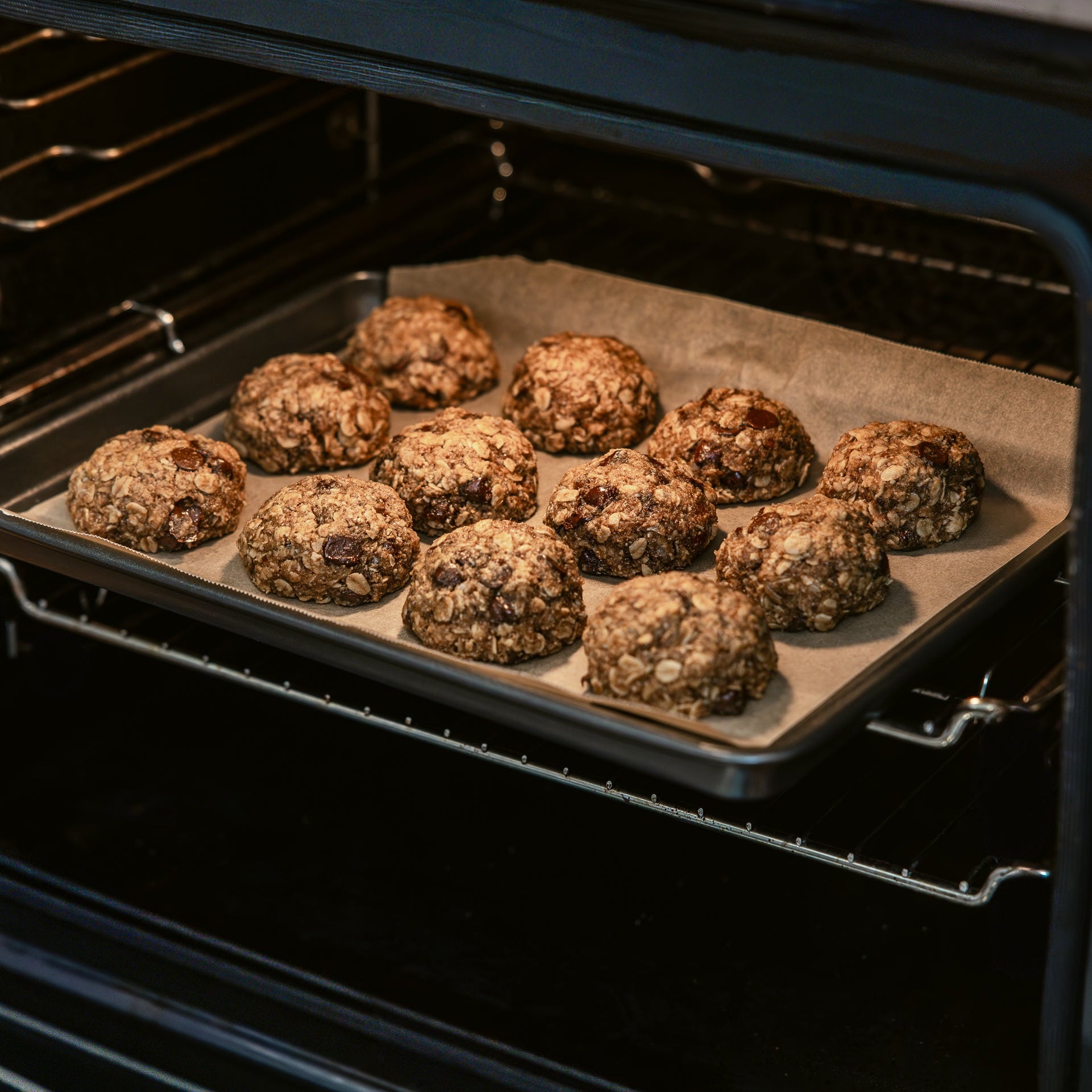 Freshly baked tray of breastfeeding biscuits with oats and dark chocolate, cooling on parchment paper.