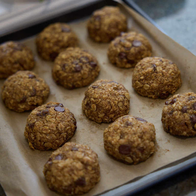 Freshly baked tray of breastfeeding biscuits with oats and dark chocolate, cooling on parchment paper.